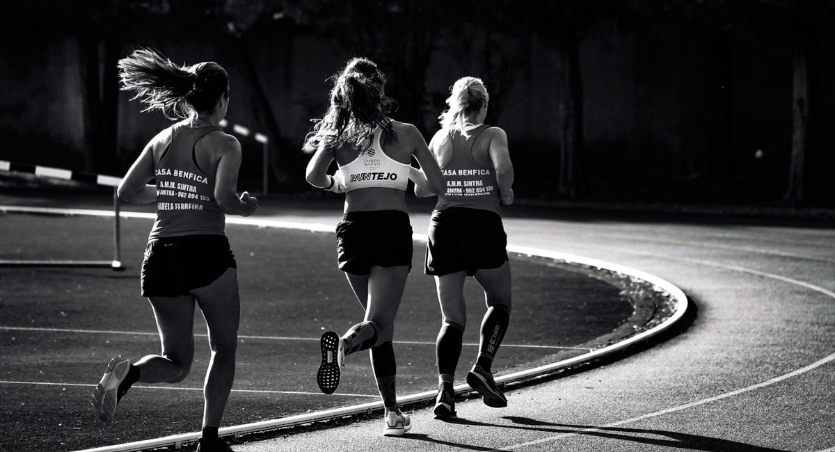 Black and white back view of unrecognizable fit female runners in sportswear running during track and field competition
