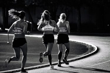 Black and white back view of unrecognizable fit female runners in sportswear running during track and field competition