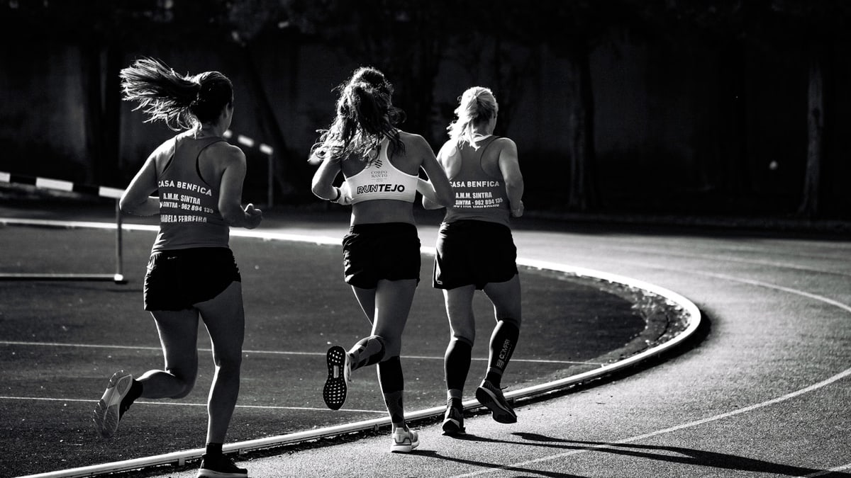 Black and white back view of unrecognizable fit female runners in sportswear running during track and field competition